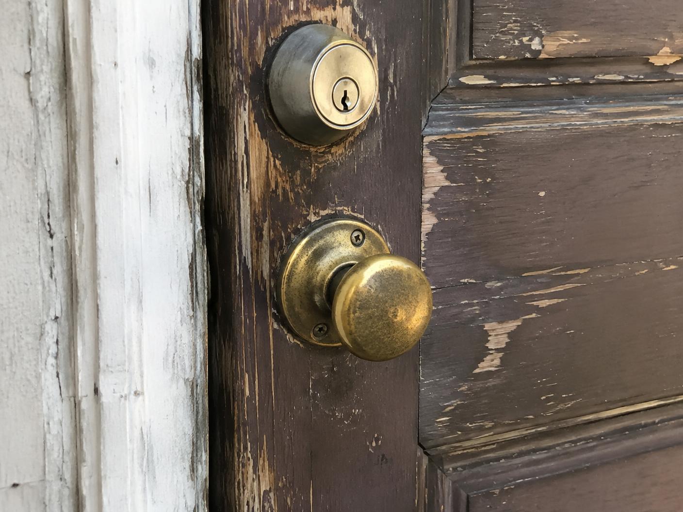 Worn brass knob and mismatched deadbolt on a weathered front door
